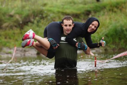 Участник грязных гонок Ural Dirty Race 2014 под Екатеринбургом  переходит речку в брод с напарницей на плечах