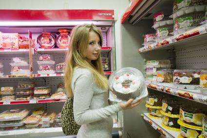 Девушка выбирает торт в кондитерском отделе магазина