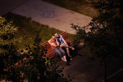 Мужчина и женщина сидят вечером на скамейке перед домом.