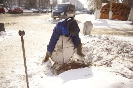 Рабочий водоканала закрывает крышкой канализационный люк