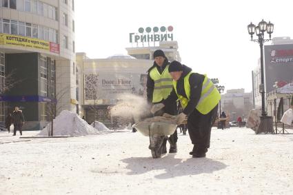 дворники разбрасывают антигололедную смесь по тротуару