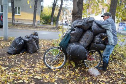 дедушка складывает на велосимед мешки с опавшими оистьями, чтобы отвезти из в сад для компоста