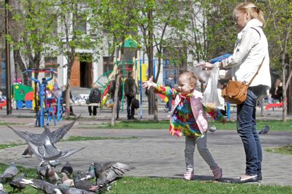 Женщина с ребенком кормят на улице голубей.