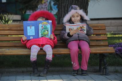 Девочки читают книги на скамейке.