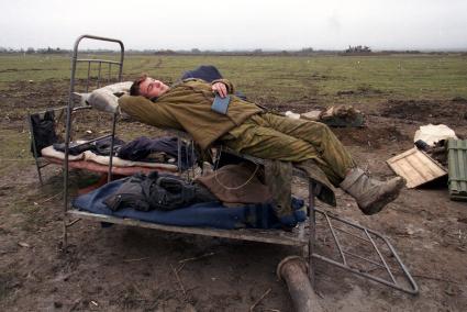 Вторая чеченская война. Урус-Мартан. Российский солдат отдыхает в поле на сломанной армейской кровати.