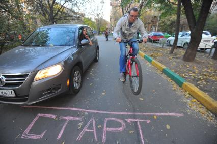 Девушка в автомобиле смотрит на проезжающего рядом мужчину на велосипеде.