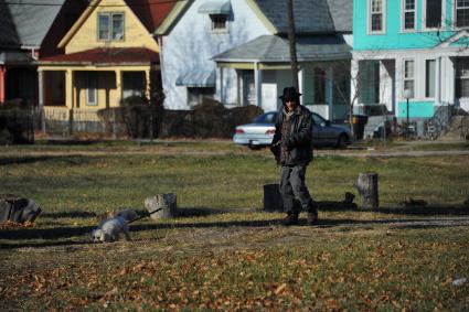 Детройт. На снимке: местный житель выгуливает собаку на поводке.