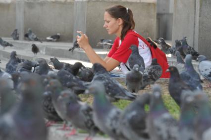 Девушка с мобильным телефоном в окружении голубей