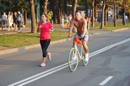 Парк Горького. На снимке: мужчина едет на велосипеде и рядом бежит девушка.
