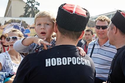 Мужчина в футболке с надписью `НОВОРОССИЯ` держит ребенка на руках на IV международном фестивале `Казачья станица`.