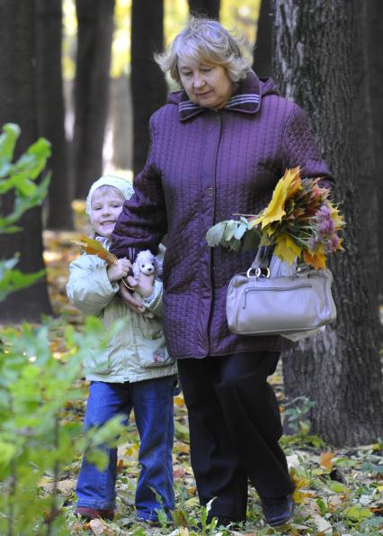Женщина и девочка собирают осенную листву в парке.