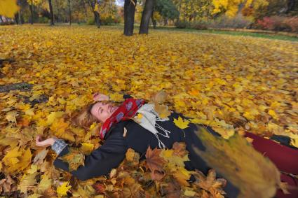 Девушка в парке лежит на желтых листьях.