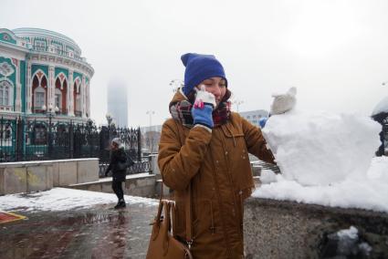 девушка говорит по телефону и катает снежный ком во время снегопада