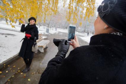 Женщины фотографируются на телефон с  желтыми листьями на дереве