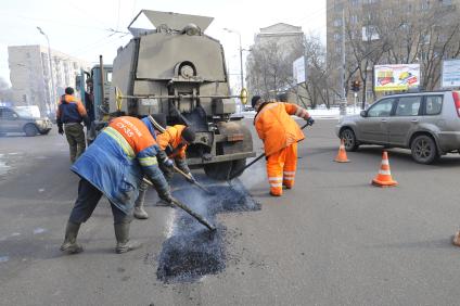 Рабочие укладывают асфальт вокруг люка на дороге.