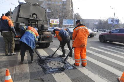 Рабочие укладывают асфальт вокруг люка на дороге.