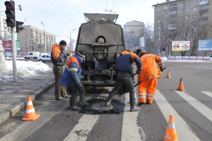 Рабочие укладывают асфальт вокруг люка на дороге.