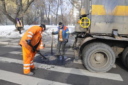 Рабочие укладывают асфальт вокруг люка на дороге.