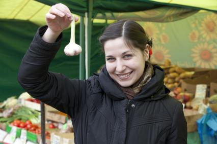 Девушка держит головку чеснока на рынке.