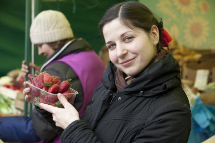 Девушка держит клубнику на рынке.
