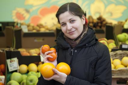 Девушка держит апельсины и помидоры на рынке.