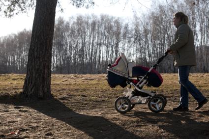 Женщина гуляет в коляской в парке.