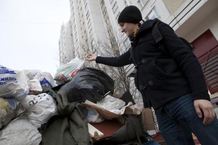 Человек выбрасывает мусор в контейнер у подъезда.