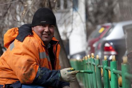 Гастарбайтеры красят забор во дворе жилого дома.