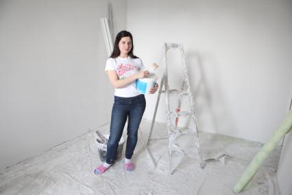Девушка держит ведро с краской и кисть на фоне ремонта