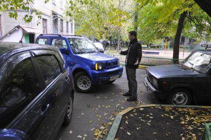 Водитель у припаркованных машин во дворе жилого дома.