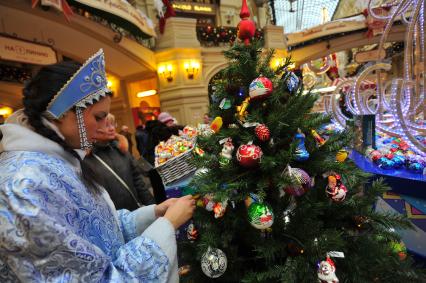 Ярмарка елочных игрушек в ГУМе. На снимке: девушка в костюме Снегурочки   украшает елку елочными шарами.