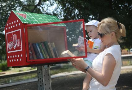 Мама с ребенком выбирает книги в уличной библиотеке организованной в краснодарском парке Городской сад.