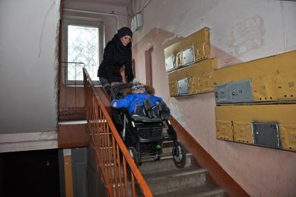 Женщина поднимает коляску по лестнице многоквартирного дома