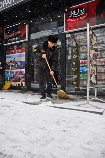 Охранник сметает снег с крыльца стрипбара, кафе и ночного клуба