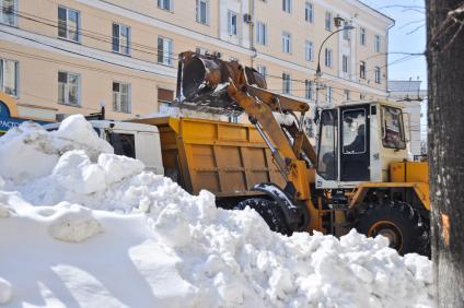 Экскаватор грузит убранный снег в кузов грузовика