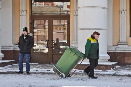 Молодой человек наблюдает, как пожилой коммунальщик везет мусорный бак