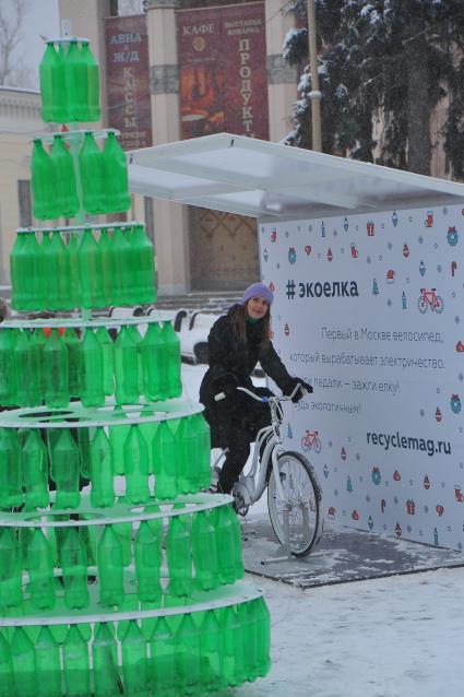 ВДНХ. Девушка на  велосипеде вырабатывающем электричество и арт-объект `Эко-елка` в городе сказок.