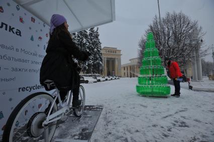 ВДНХ. Девушка на  велосипеде вырабатывающем электричество и арт-объект `Эко-елка` в городе сказок.