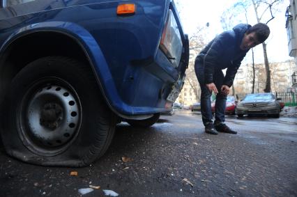 Парковка автомобилей. На снимке: мужчина смотрит  на спущенное  колесо автомобиля.