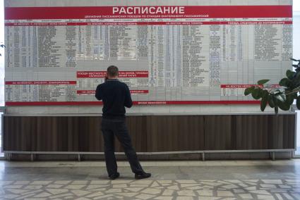 мужчина смотрит расписание поездов по станции Екатеринбург-пассажирский в зале ожидания на железнодорожном вокзале в Екатеринбурге