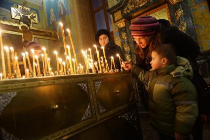 Женщина помогает ребенку поставить свечу во время  Рождественской службы. Свято-Троицкий кафедральный собор в Екатеринбурге