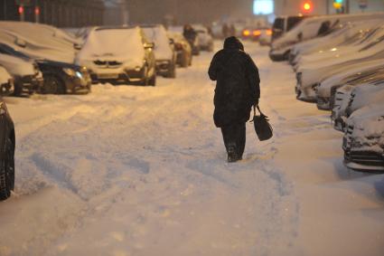 Последствия снегопада в Москве. На снимке: женщина идет мимо заснеженных машин.