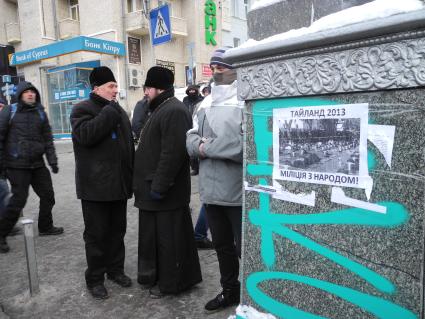 Киев. Священники разговаривают рядом с плакатом `Таиланд 2013 - милиция с народом!` у площади Независимости.