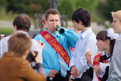 выпускник пьет пиво из бутылки, во время празднования последнего звонка. Набережная Исети в Екатеринбурге.