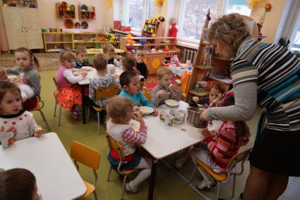 воспитатель кормит детей в детском саду
