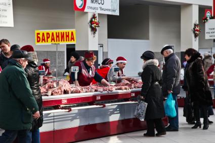 Продавщица баранины показывает мясо покупателям