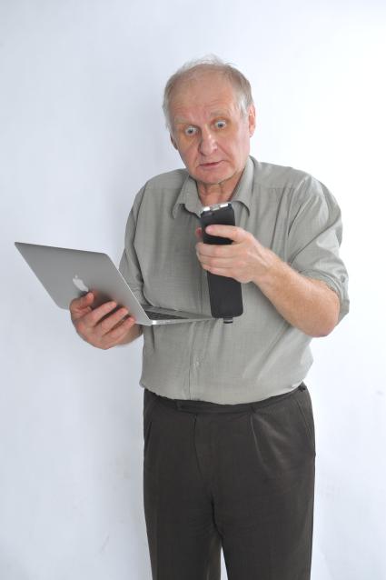 Мужчина держит в руках ноутбук и мобильный телефон.