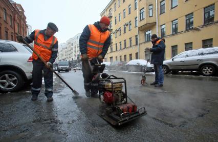 Санкт-Петербург. Ремонт асфальта. На снимке: рабочий укладывает асфальт с помощью виброплиты.