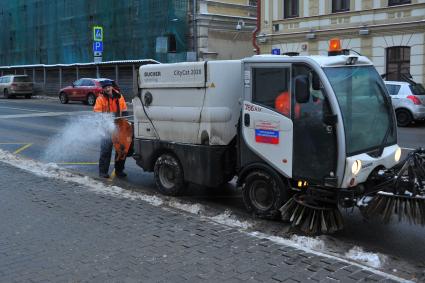 Работник жилищно-коммунального хозяйства посыпает пешеходную зону реагентом.