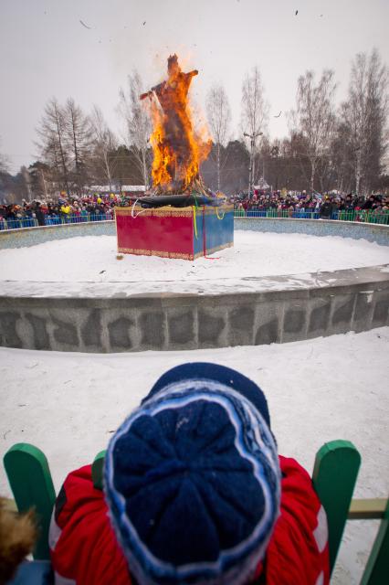 ребенок наблюдает за горящим чучелом зимы, во время празднования масленицы в Екатеринбурге